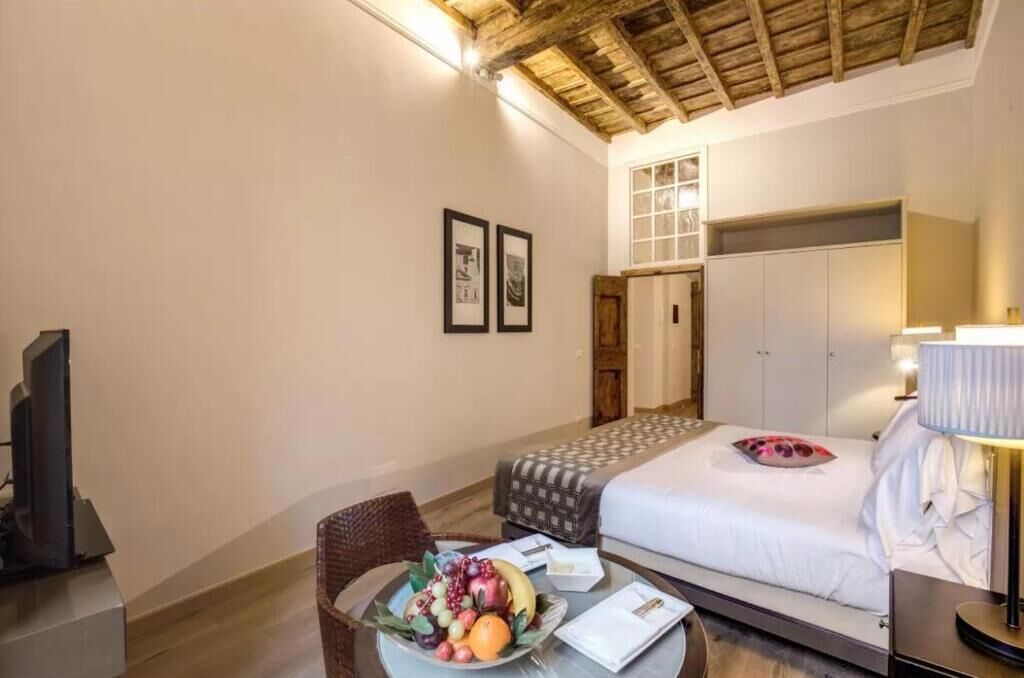 A hotel room with a bed, a television, a dining table with fruit, and a wooden ceiling.