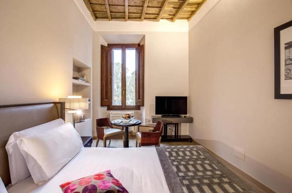 A hotel room with a bed, a desk with a chair, a television, and a window with wooden shutters.