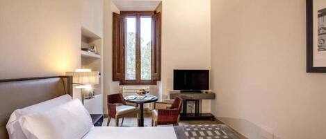 A hotel room with a bed, a desk with a chair, a television, and a window with wooden shutters.