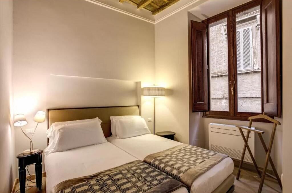 Habitación de hotel con dos camas, un calentador portátil, una ventana con persianas y una lámpara en la mesita de noche.
