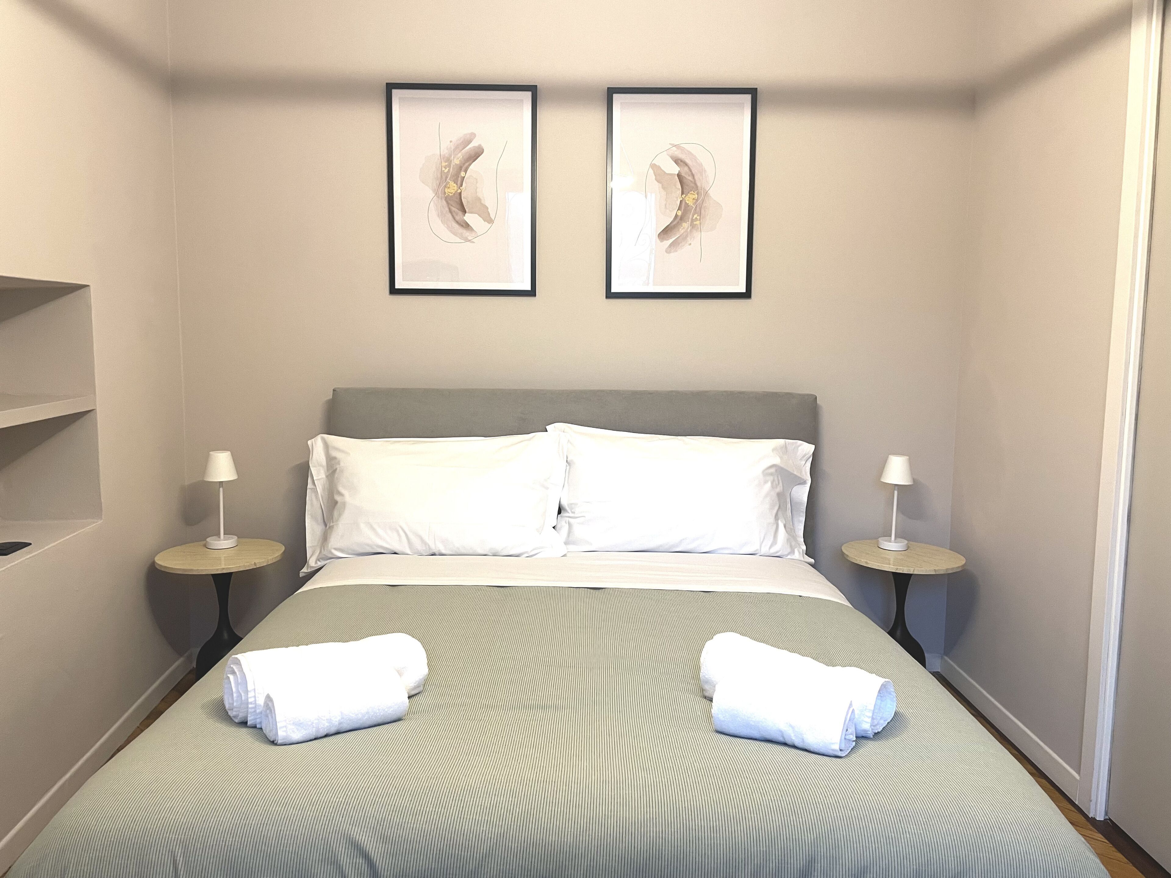 Een hotelkamer met een bed, twee nachtkastjes, twee lampen, twee ingelijste kunstwerken en twee opgerolde handdoeken.