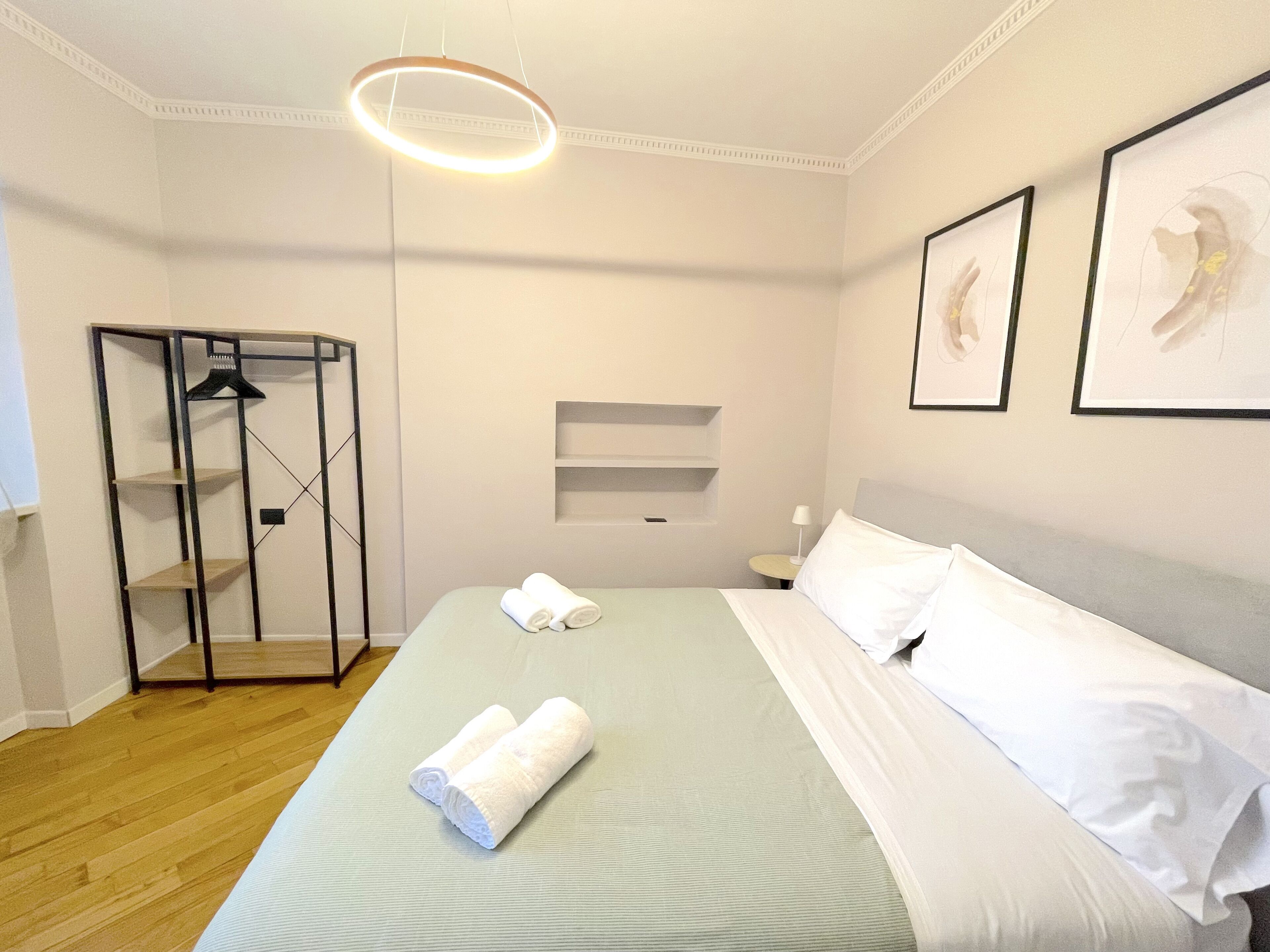 A hotel room with a bed, a wardrobe, a hanging light fixture, and two framed pictures on the wall.