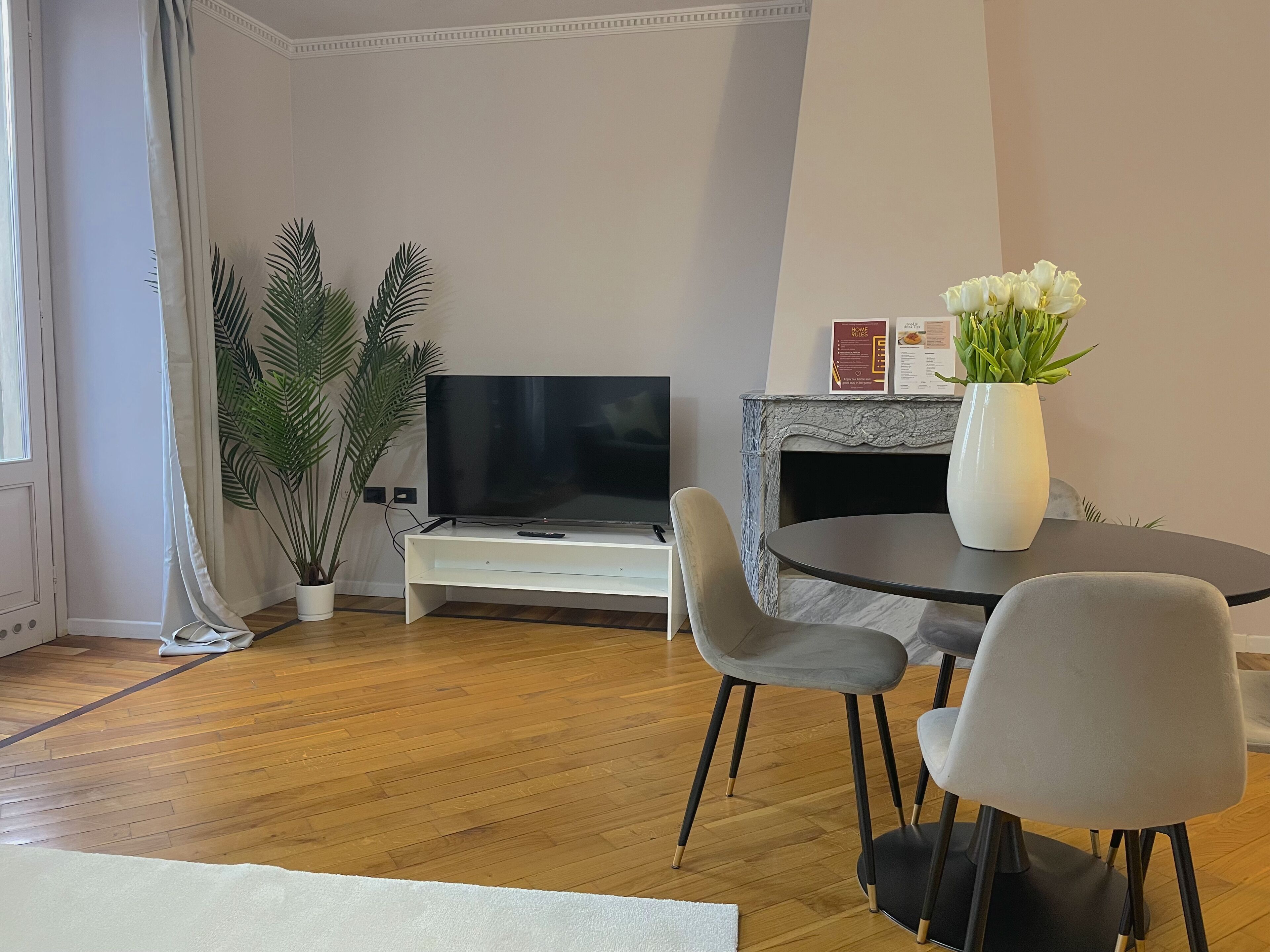 A modern living room with a flat-screen TV, a round table with chairs, a potted plant, and a decorative vase.