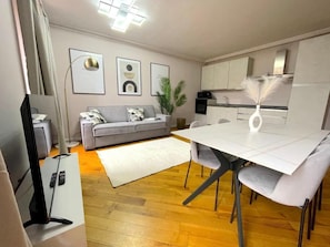 A modern living room with a grey sofa, a dining table with chairs, a flat-screen TV, and a kitchen area with cabinets and a microwave. - Best View Boutique Apartments  (Bergamo)