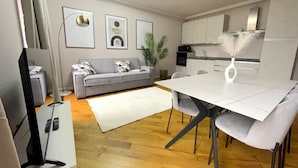 A modern living room with a grey sofa, a dining table with chairs, a flat-screen TV, and framed artwork on the wall. - Best View Boutique Apartments  (Bergamo)