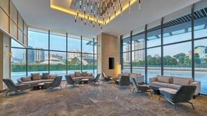 Un vestíbulo moderno con ventanas amplias, un área de estar con sofás y sillones, y piso de mármol.