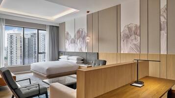 A modern hotel room with a large bed, a desk, and a view of tall buildings.