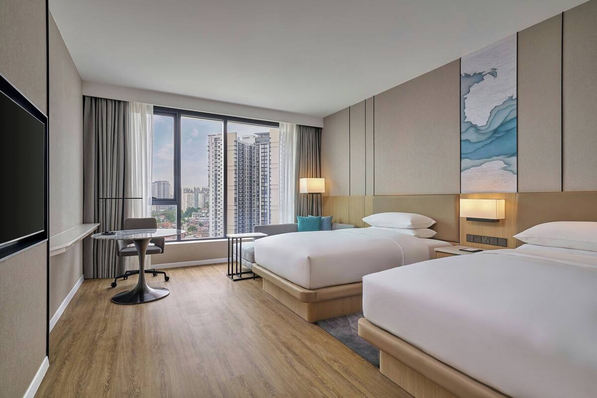 Une chambre d’hôtel avec deux lits, un bureau et une grande fenêtre donnant sur la ville.
