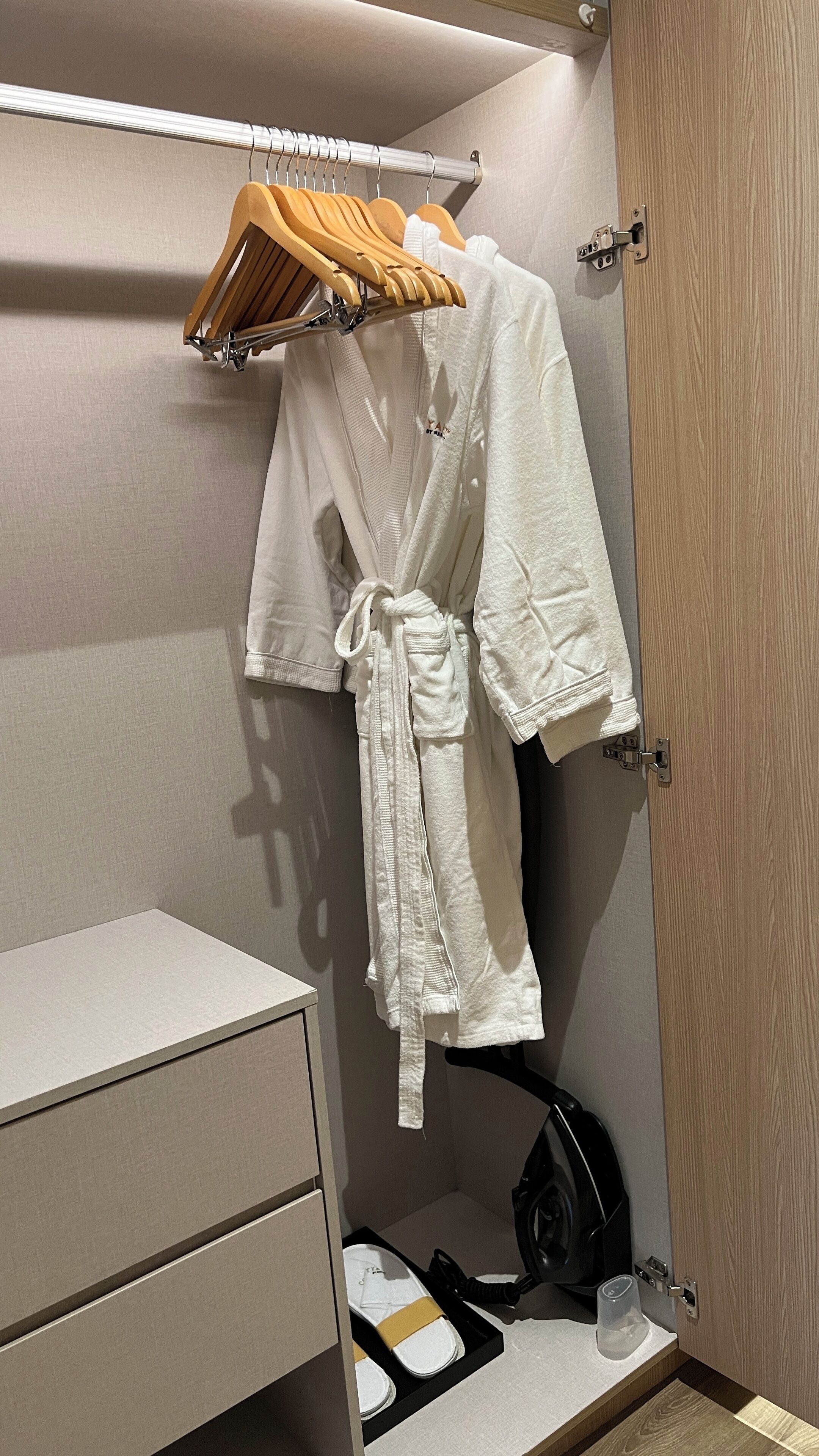 A bathroom with a wooden hanger rack holding a white robe, a black vacuum cleaner, and a pair of slippers on a tray.