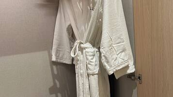 A bathroom with a wooden hanger rack holding a white robe, a black vacuum cleaner, and a pair of slippers on a tray.
