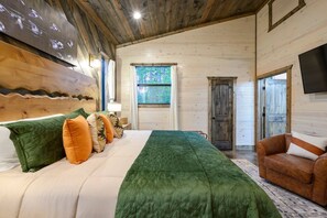 A wooden cabin bedroom with a bed, pillows, a green blanket, a wooden door, and a TV on the wall.