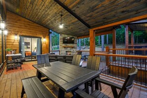 A wooden deck with a dining table and chairs, a stone fireplace, and a TV mounted on the wall.