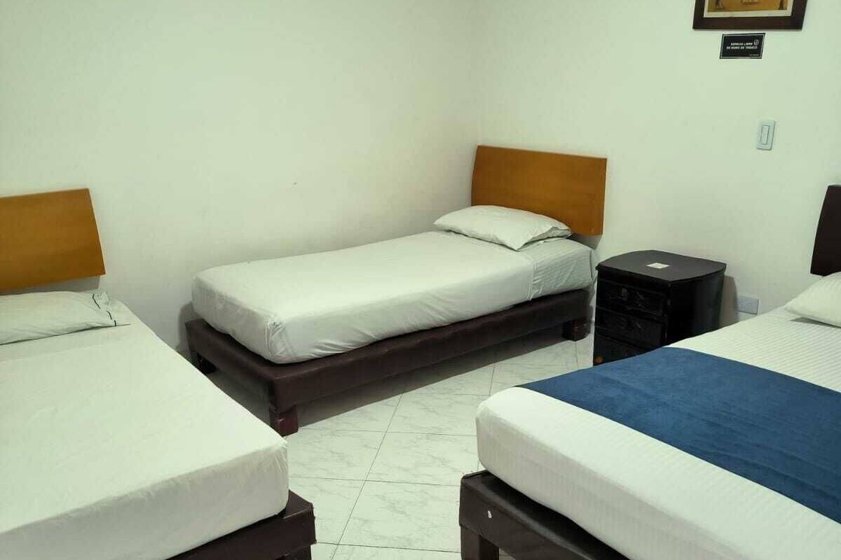 A hotel room with three single beds, a small black nightstand, and a framed picture on the wall.