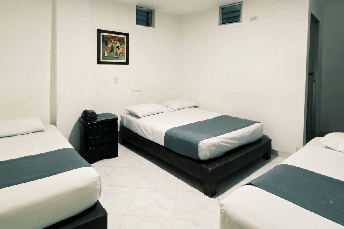 A bedroom with two beds, a bedside table, a small painting, and a window.