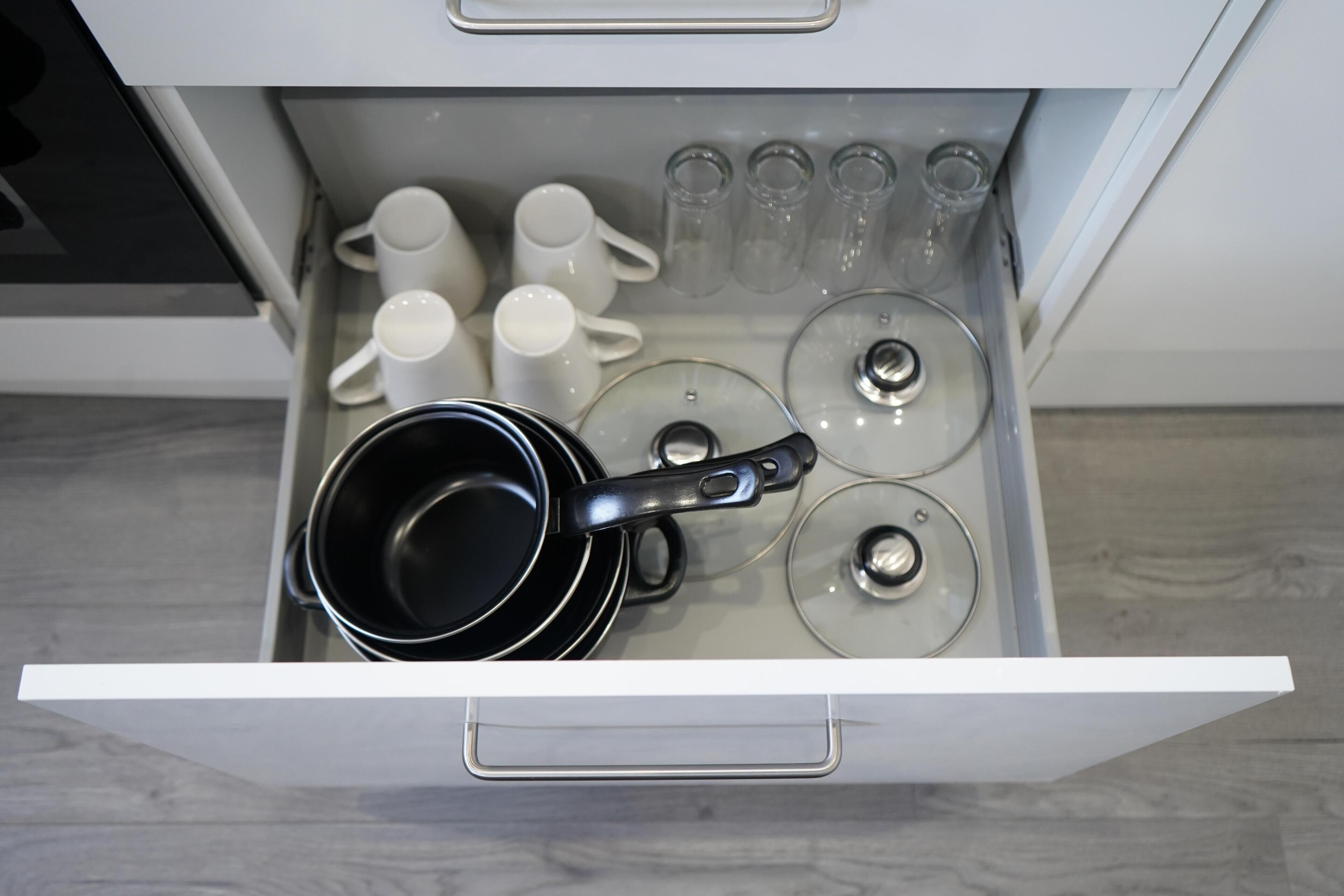 A kitchen drawer with a black pot, white mugs, and clear glass cups.