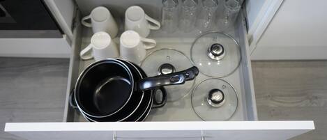 A kitchen drawer with a black pot, white mugs, and clear glass cups.