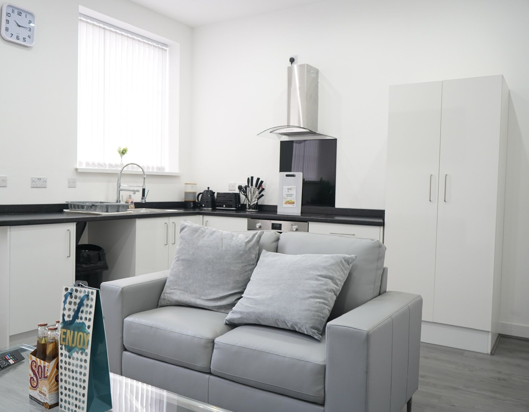 A modern kitchen with a grey sofa, white cabinets, and a stainless steel range hood.