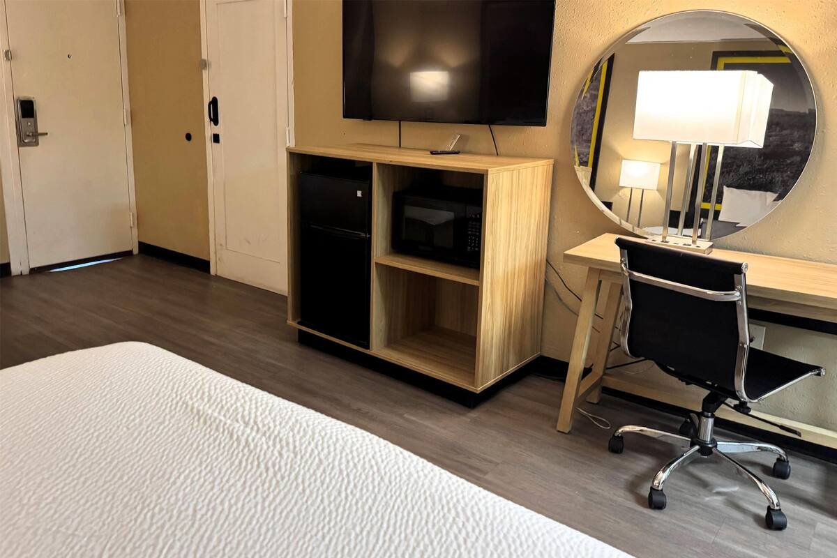 A hotel room with a bed, a desk with a chair, a television, a microwave, and a mirror.