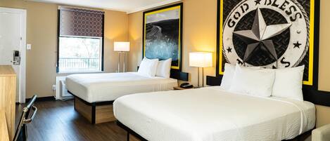 A hotel room with two beds, a large window, and a wall with a 'God Bless' sign.