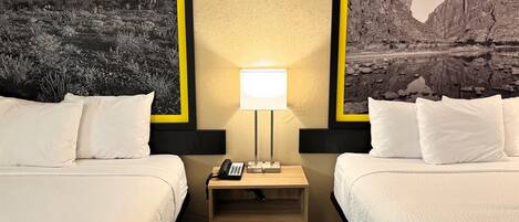 Habitación de hotel con dos camas, una mesita de noche con lámpara, un teléfono y un mural en la pared que representa un paisaje desértico.