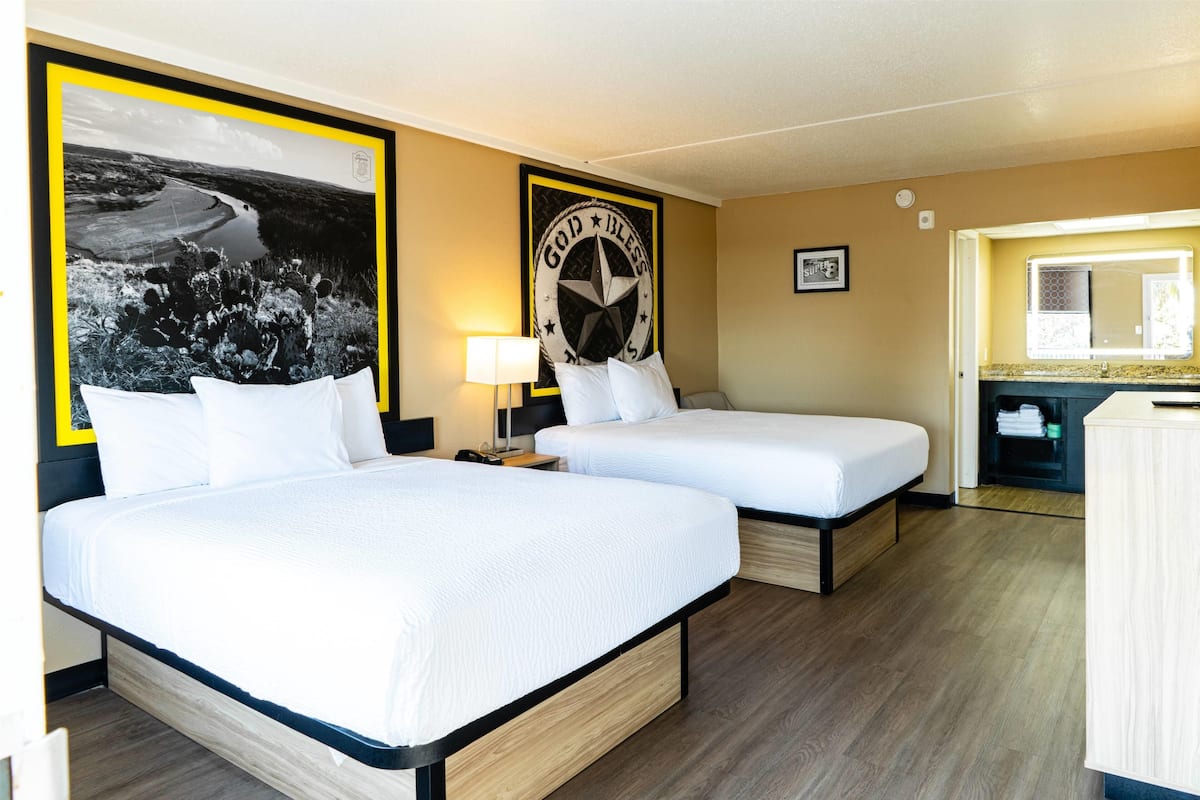 A hotel room with two beds, a large framed picture of a landscape, a wall clock, and a small window.