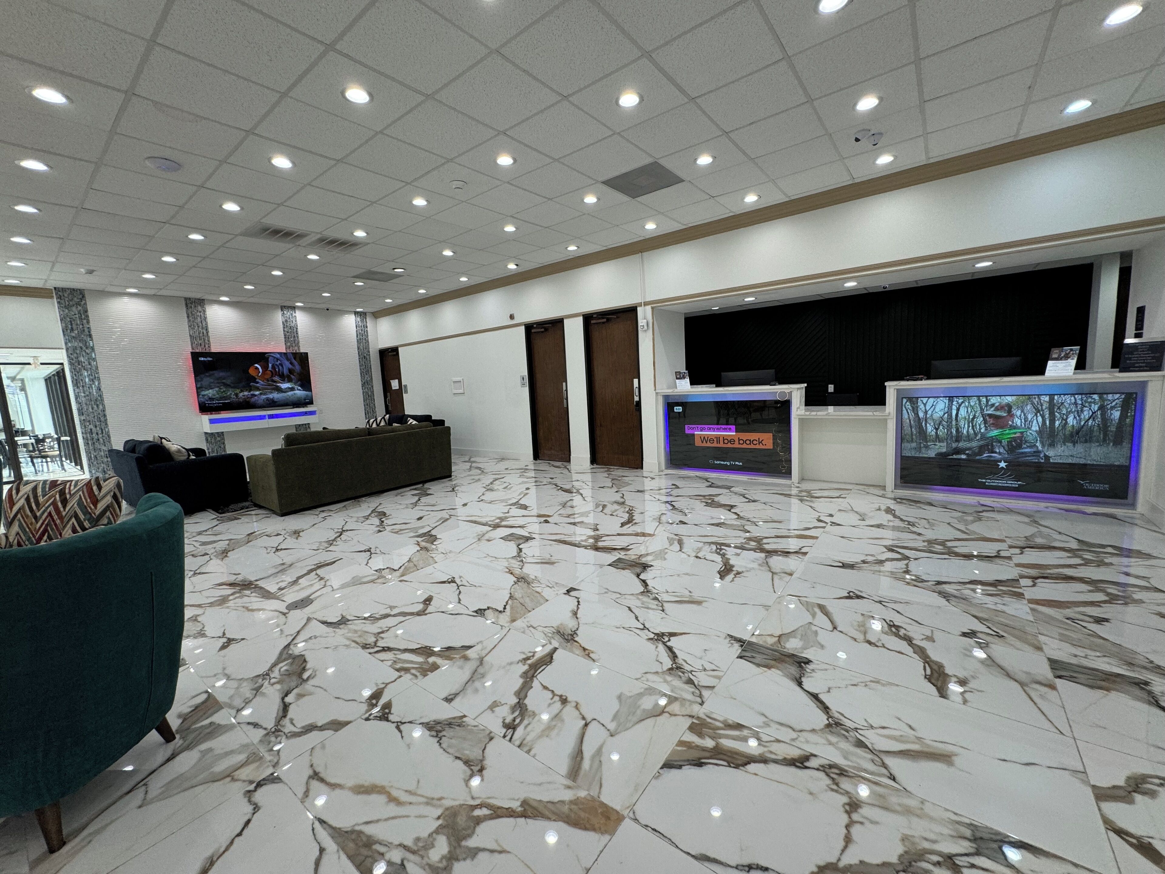 Un amplio hall de entrada con piso de mármol, un mostrador de recepción, un televisor y áreas de descanso.