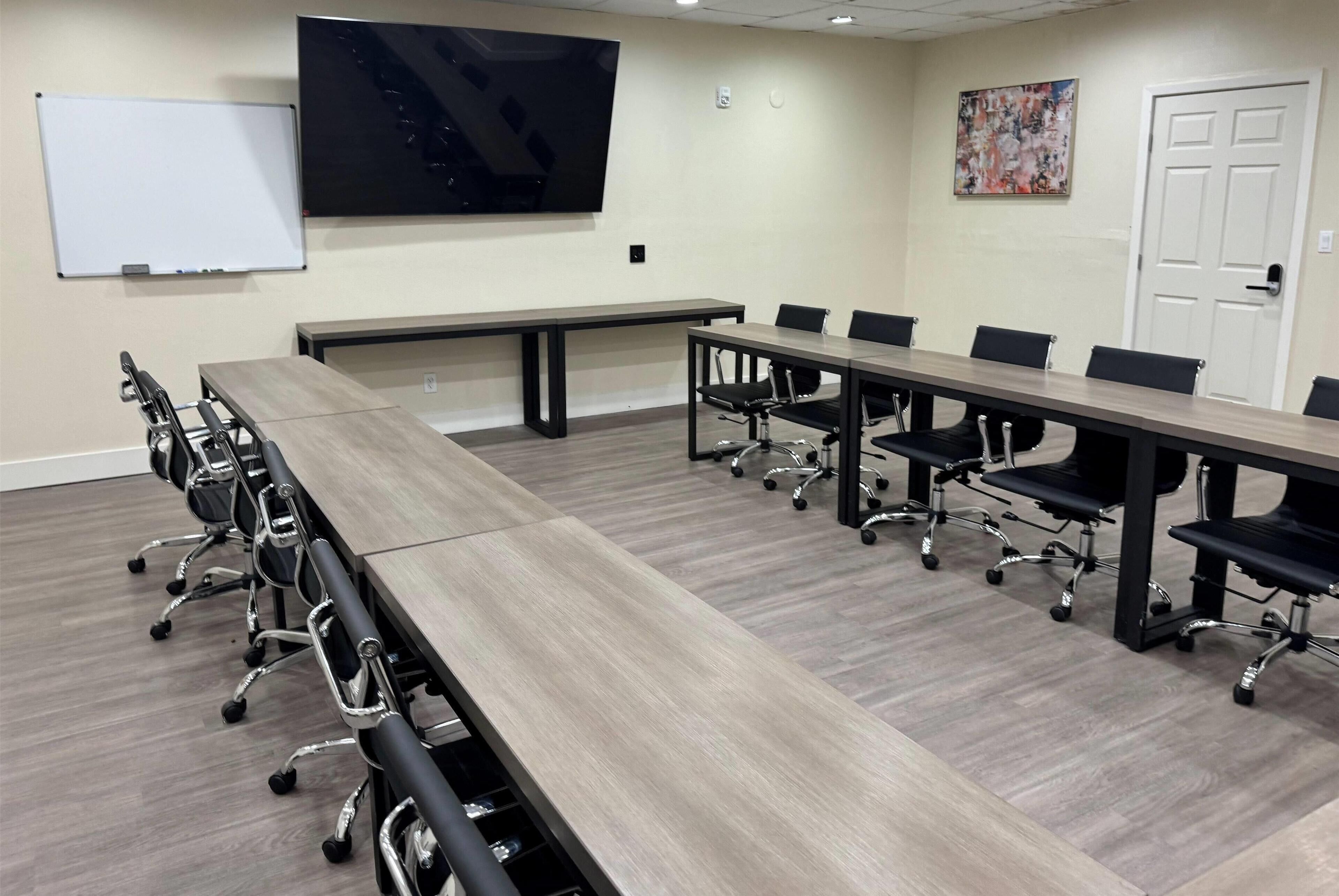 A conference room with a long table, chairs, a whiteboard, a TV, and a door.