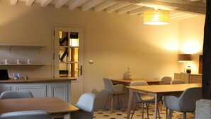 A dining area with a wooden table and chairs, a kitchen area with a counter and shelves, and a staircase leading to an upper level.