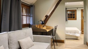 A room with a sofa, a desk with a lamp, a bed, and a window with curtains.
