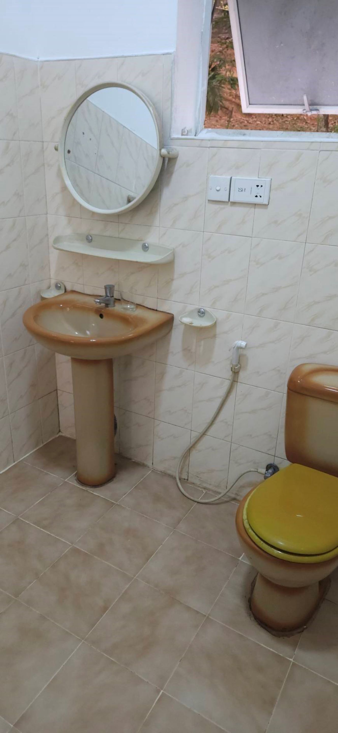 A bathroom with a beige sink, a mirror, a toilet, and a window.