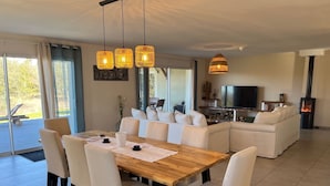 A modern living room with a wooden dining table, white sofas, and a TV. - Villa Spacieuse Avec Piscine, 3 Chambres, Proche Ardèche, Grotte Aven D'orgnac (Issirac)