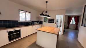A modern kitchen with a central island, built-in oven, microwave, and black pendant lighting. - Villa Spacieuse Avec Piscine, 3 Chambres, Proche Ardèche, Grotte Aven D'orgnac (Issirac)
