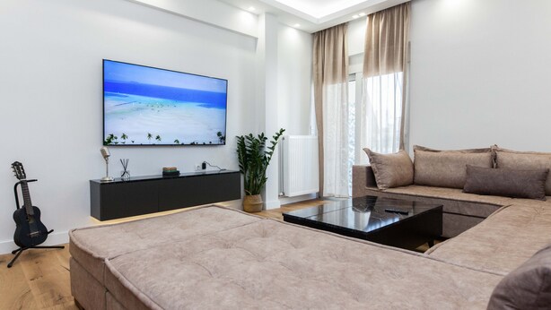 A modern living room with a large flat-screen TV, a sofa, a coffee table, and a guitar. - Kallithea Modern Living w Designer Touch (Kallithea)