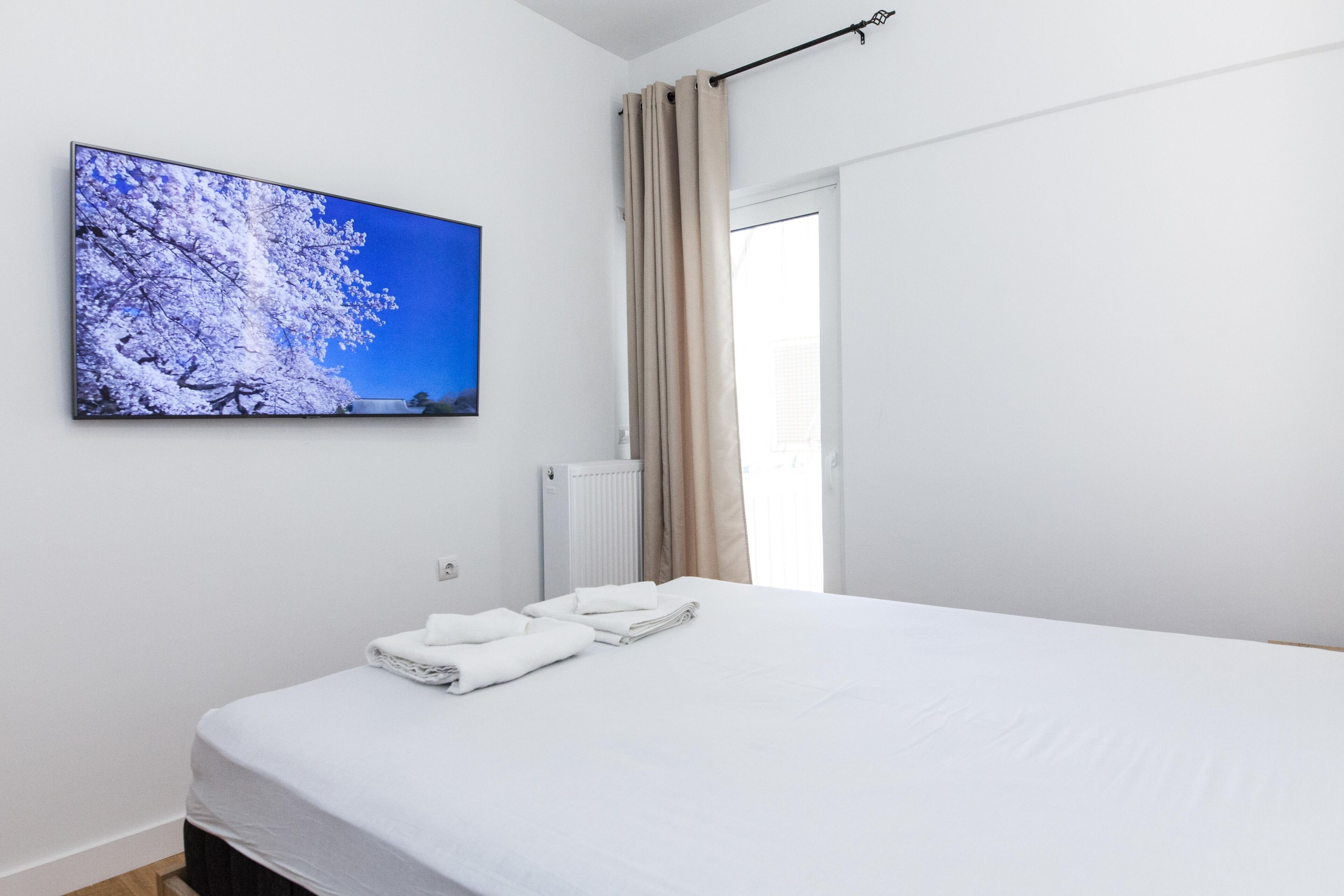 Une chambre à coucher avec un lit, une fenêtre avec des rideaux, un radiateur et un téléviseur fixé au mur qui diffuse une image d’un paysage enneigé.