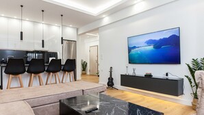 A modern living room with a large TV, a marble coffee table, and a seating area with a sofa and chairs. - Kallithea Modern Living w Designer Touch (Kallithea)