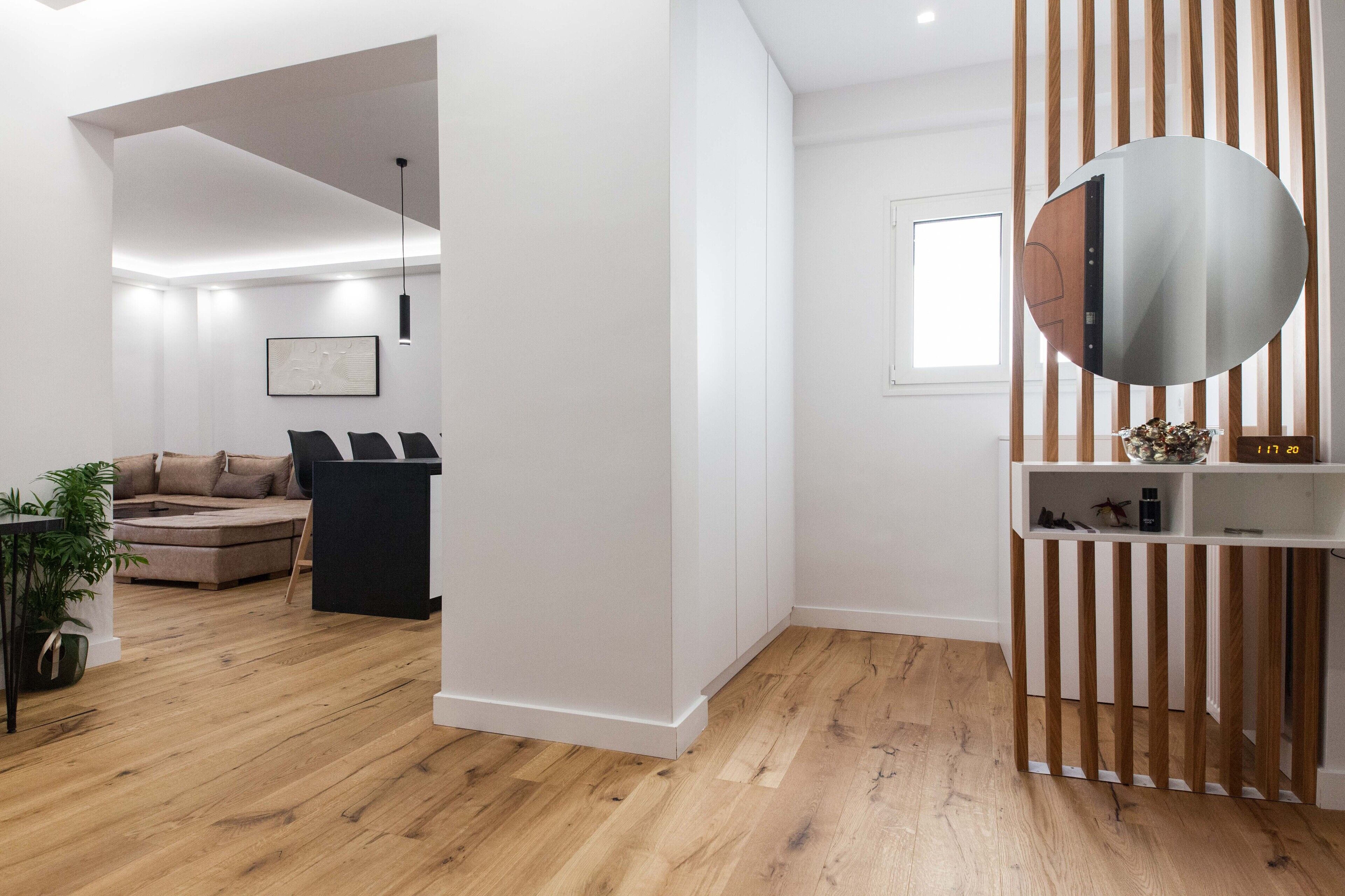 A modern living room with a wooden floor, a black sofa, a white wall, and a round mirror.