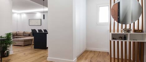 A modern living room with a wooden floor, a black sofa, a white wall, and a round mirror.