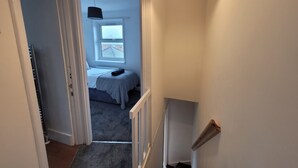 Un pasillo estrecho que conduce a un dormitorio con cama, ventana e iluminación en el techo.