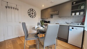 Una cocina moderna con armarios grises, un lavavajillas y una zona de comedor con dos sillas y una mesa.