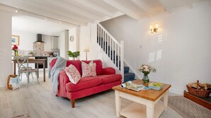 A spacious living room with a red sofa, a wooden coffee table, and a staircase leading to a kitchen. - Lavender Cottage -  a cottage that sleeps 2 guests  in 1 bedroom (Portscatho)