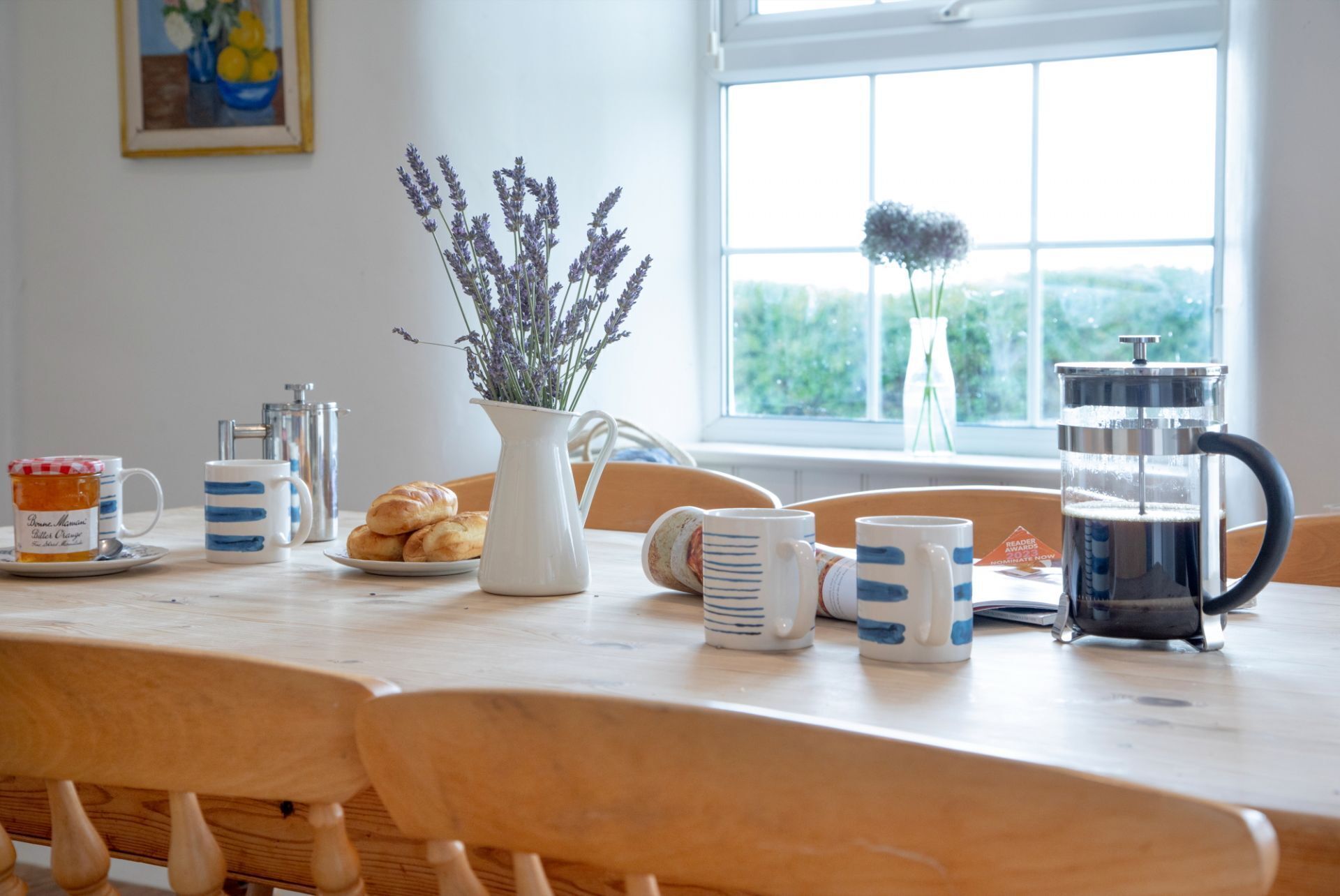 A breakfast table with a coffee maker, a pitcher, and a vase with flowers.