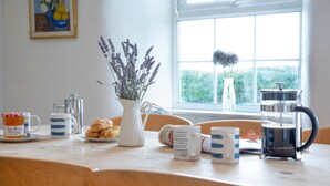 Ein Frühstückstisch mit Kaffeemaschine, Karaffe und Blumen in einer Vase.