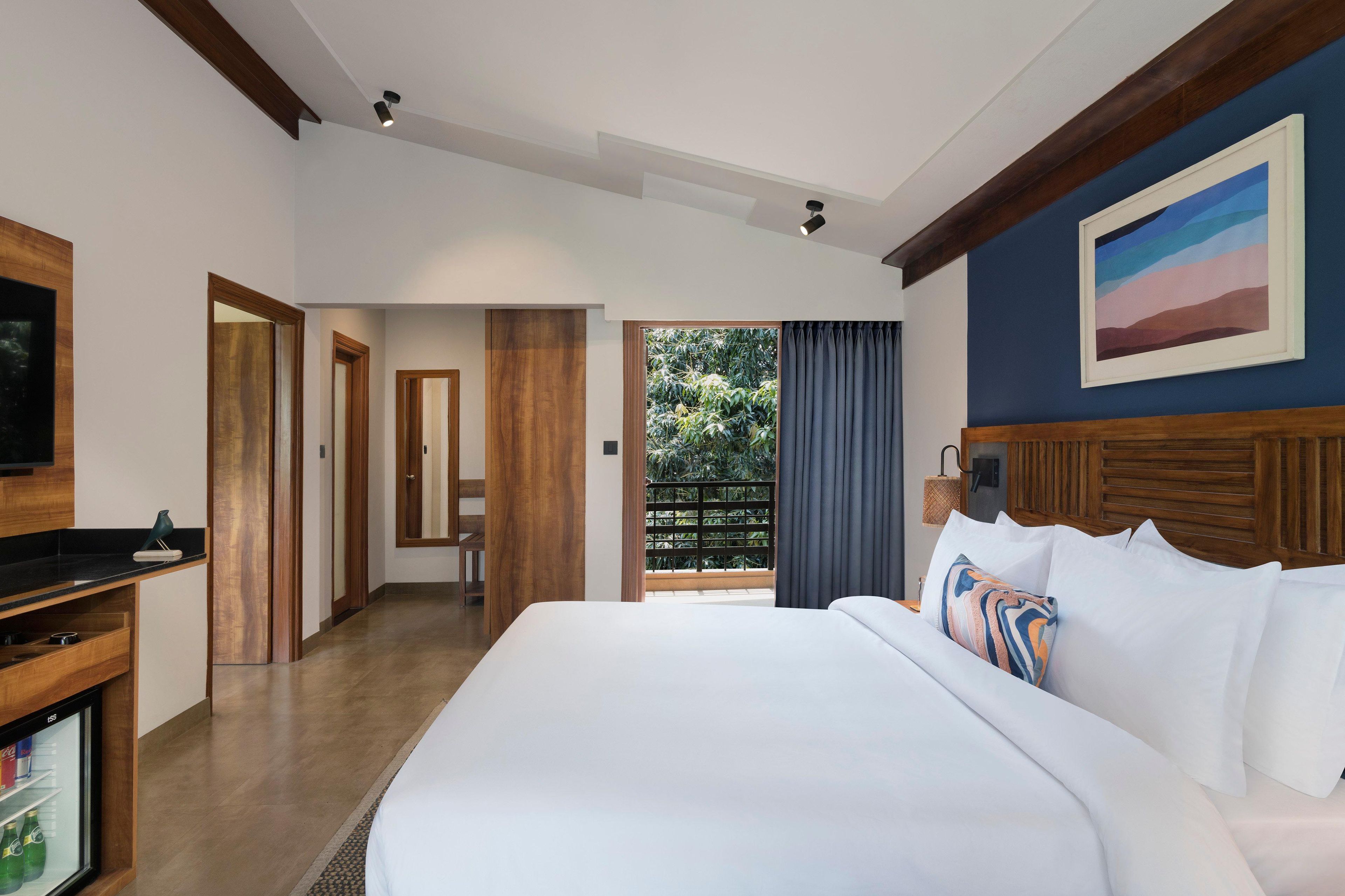 Habitación de hotel con una cama grande, un escritorio con computadora, televisor y vistas al exterior con áreas verdes.