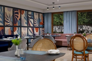 Un restaurant moderne agrémenté d’une fresque murale abstraite et colorée, doté de sièges confortables et offrant une vue sur la verdure environnante.