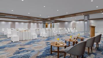 Un salón de conferencias con mesas redondas, sillas blancas y un atril.