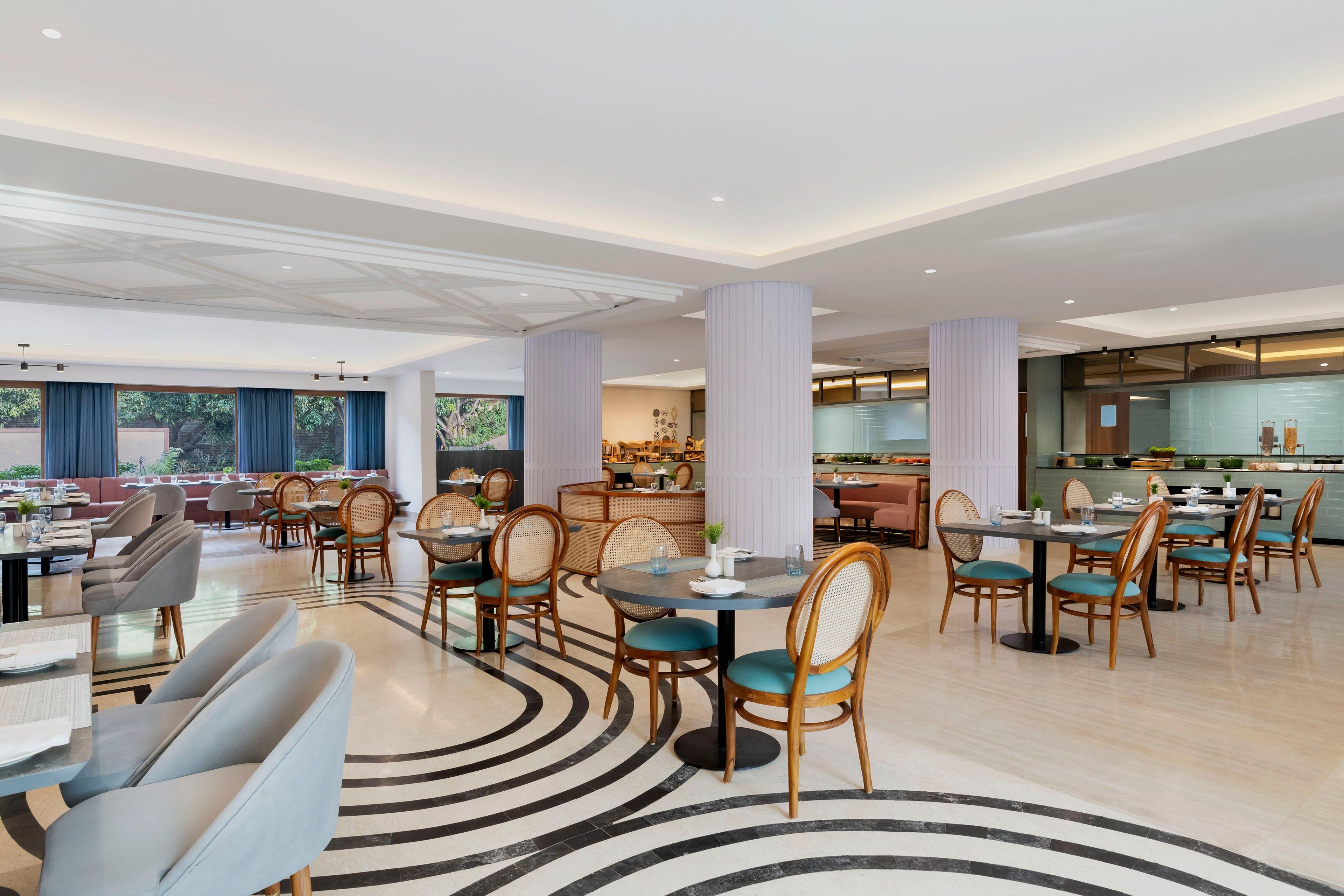 Eine moderne Hotelhalle mit runden Tischen, bequemen Sitzgelegenheiten und einer zentralen Empfangstheke mit Sitzplätzen.