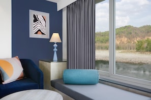 Une pièce avec vue sur une rivière et des collines, un canapé bleu, une lampe et une œuvre d’art encadrée au mur.