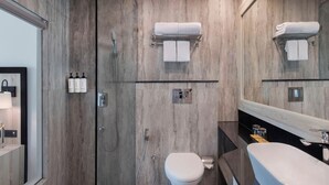 A modern bathroom with a wooden vanity, a large mirror, a toilet, and a shower area. - Voco Jim Corbett (Ramnagar)