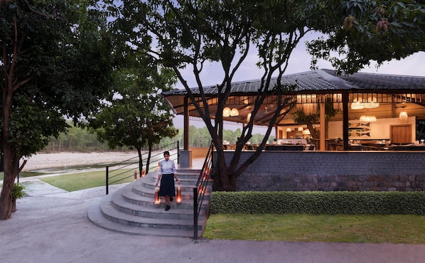 A restaurant with outdoor seating, a staircase leading up to it, and a view of the surrounding landscape. - Voco Jim Corbett (Ramnagar)