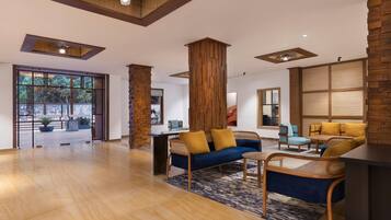 A spacious lobby with a wooden floor, a blue sofa with yellow cushions, and a rattan chair.